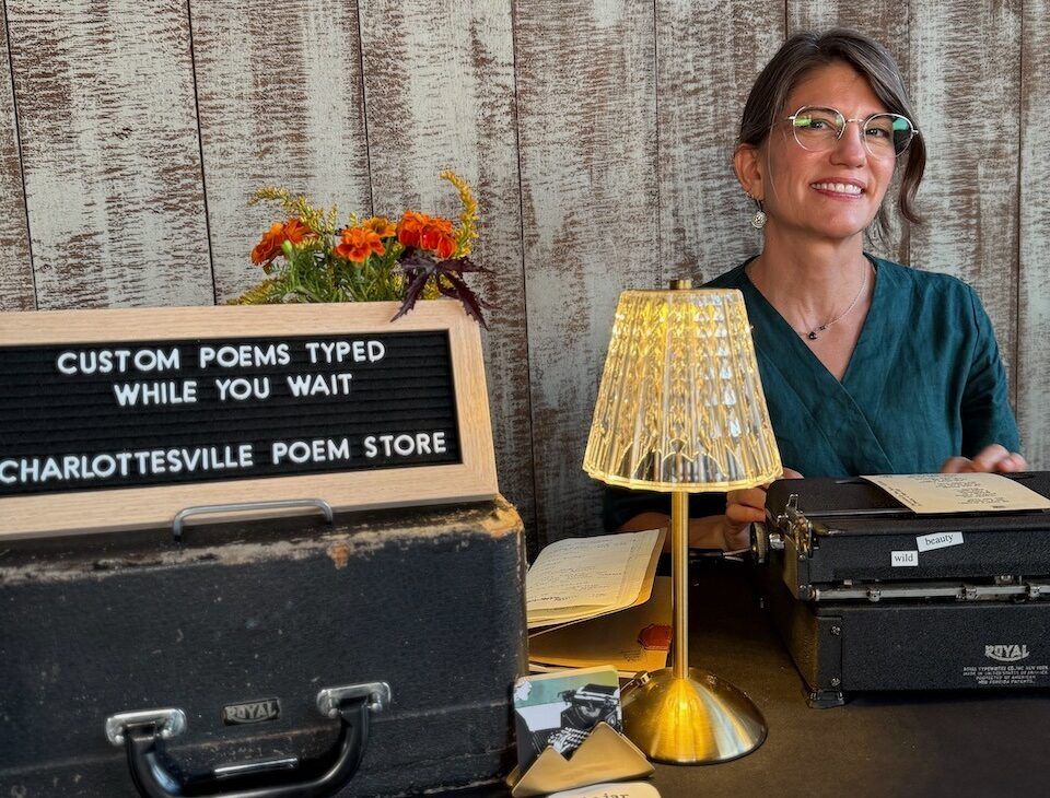 Laura Frantz at a Charlottesville Poem Store typewriter table with a sign reading Custom Poems Typed While You Wait