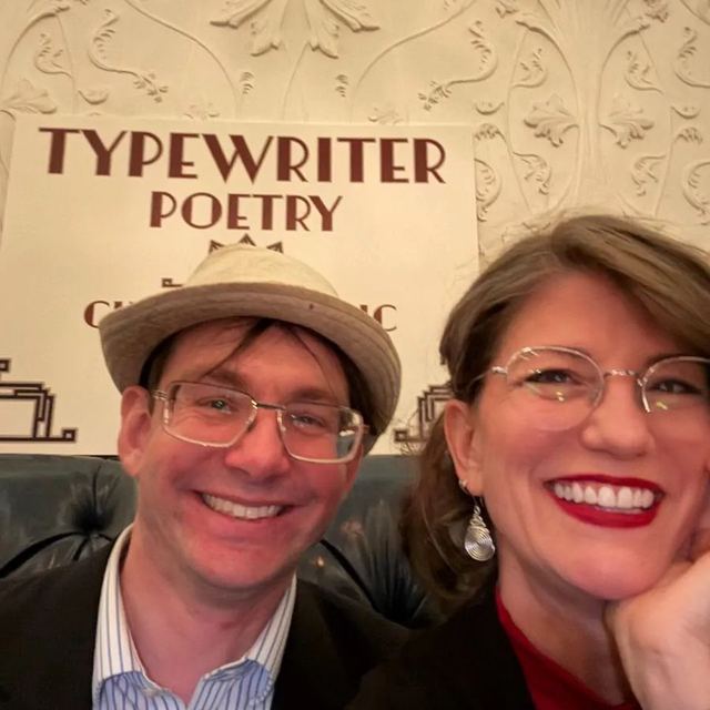 Two smiling people under a Typewriter Poetry sign at a Charlottesville Poem Store event