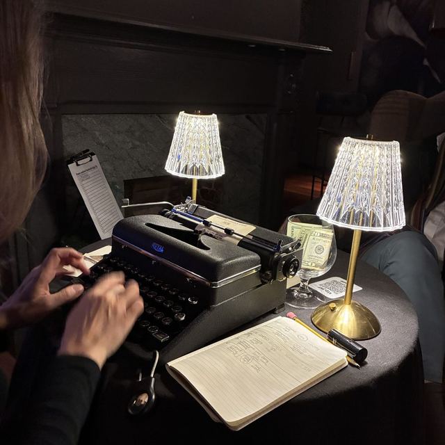 Hands typing a custom poem on a vintage typewriter between two crystal lamps