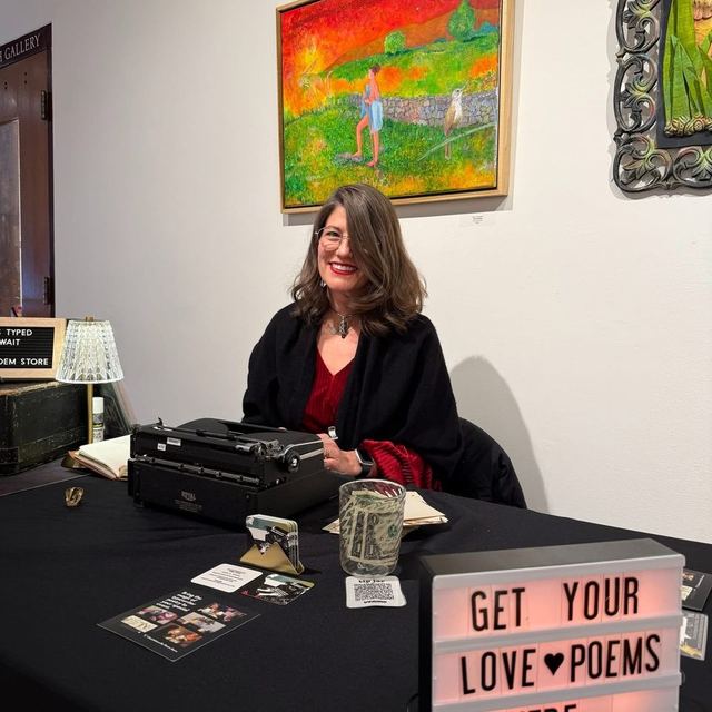 Typewriter poet at a gallery event table with a Get Your Love Poems sign