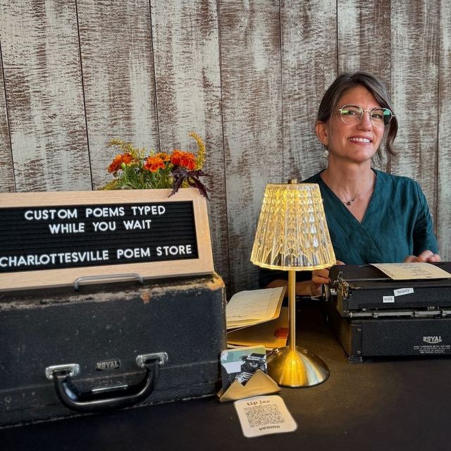 Poet at a Charlottesville Poem Store table with a Custom Poems Typed While You Wait sign