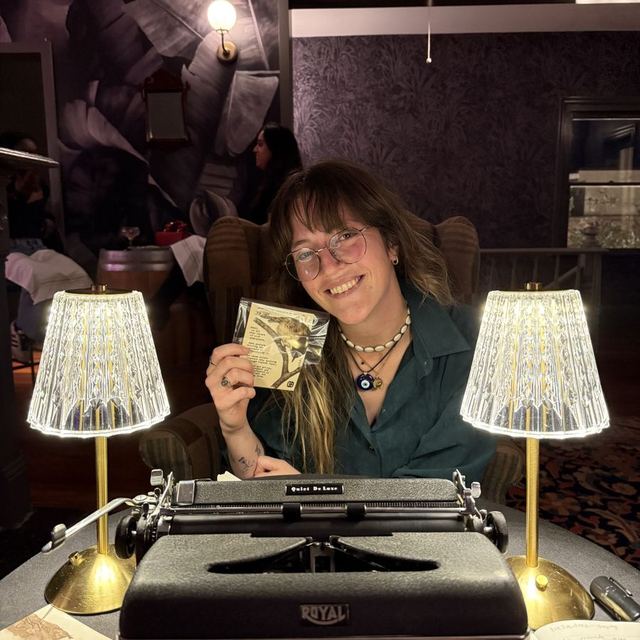 A guest holding her typewritten poem behind a Royal typewriter at Poem-crafted Cocktails at Speakeasy & Whiskey Bar